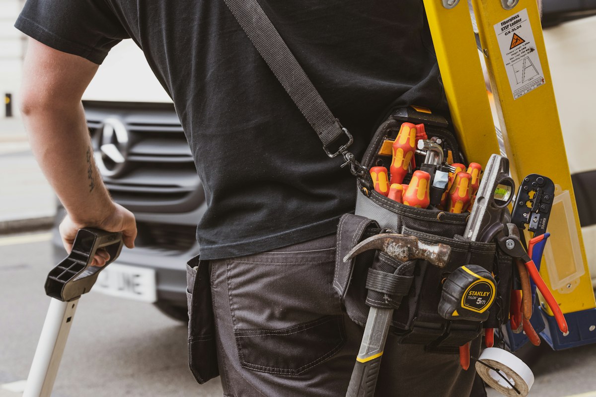 A tradesperson with a tool belt beside a work van